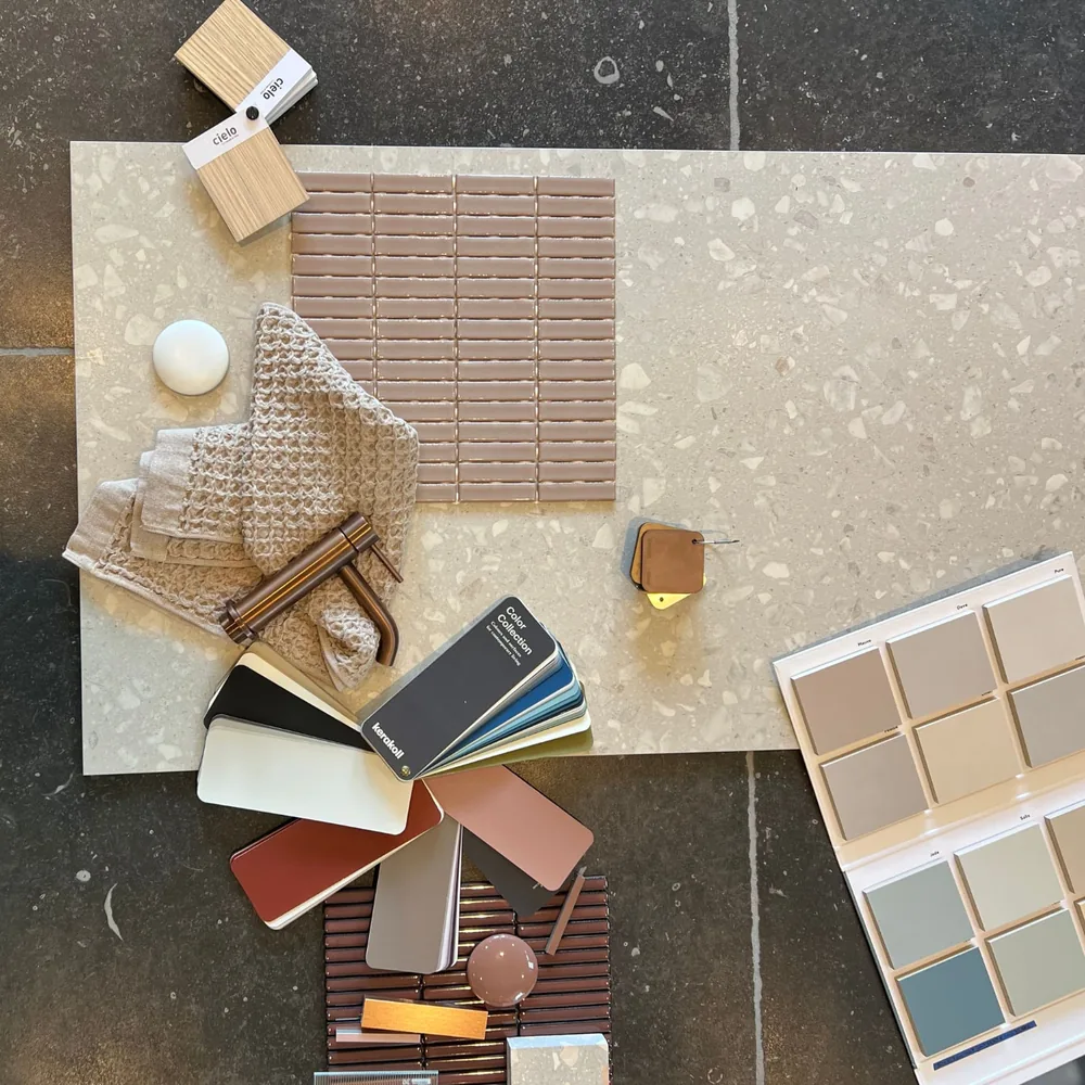 Moodboard mit Terrazzoplatte, beigem Handtuch, bronzefarbener Armatur und Farbfächern