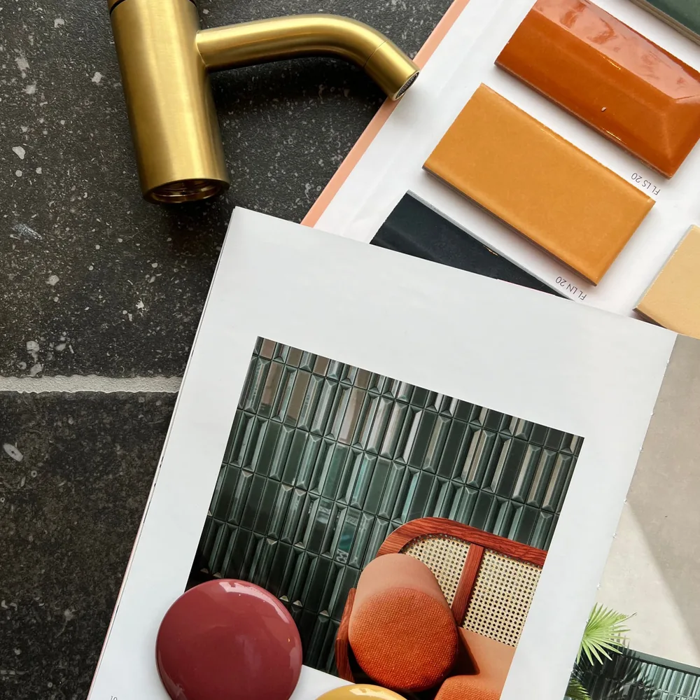 Goldfarbene Armatur neben orangefarbenen Fliesenproben und einem aufgeschlagenen Magazin