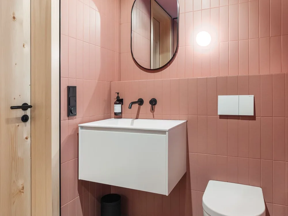 Gäste-WC mit altrosa Wandfliesen, weißem Waschtischunterschrank, ovalem Spiegel und wandhängendem WC